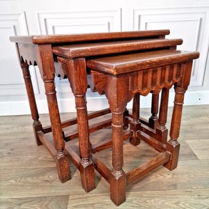 May include: A set of three antique nesting tables in dark wood. The tables have rectangular tops and carved aprons. The legs are turned and connected by stretchers. The largest table is approximately 61 cm wide, 41 cm deep, and 51 cm tall.