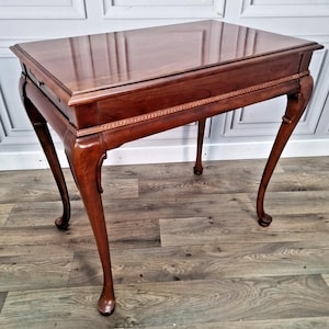 May include: A mahogany antique table with a rectangular top and four curved legs. The table has a decorative border along the apron and a glossy finish. The legs end in a ball and claw foot design. The table is approximately 76 cm long.