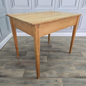 May include: A rectangular wooden table with a light brown natural wood grain finish. The table features a flat top surface and four straight, slightly tapered legs that extend downwards from the corners, providing a stable base for the structure.