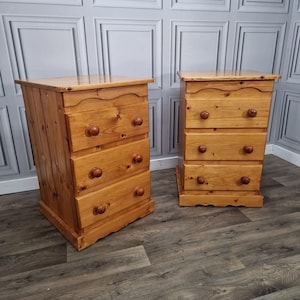 May include: Two wooden chests of drawers, each with four drawers and rounded wooden knobs. The light-coloured wood has a natural finish. The dressers are side by side on a wooden floor.