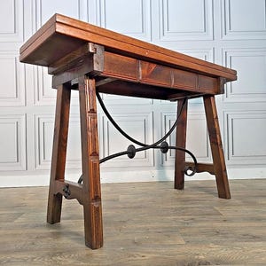 May include: A wooden console table with a dark brown finish. The table has a rectangular top, a drawer, and angled legs. A black metal support with decorative scrolls connects the legs. The table is approximately 102 cm long.