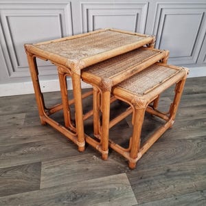 May include: A set of three nesting tables made from light brown bamboo with woven rattan tops. The tables are rectangular with rounded corners and a natural finish. The largest table is approximately 61 cm wide, 46 cm deep, and 51 cm tall.