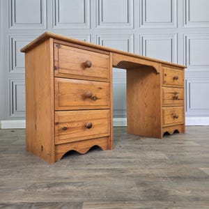 May include: A light brown wooden desk featuring a rectangular top and two pedestals. The left pedestal has three stacked drawers with round wooden knobs, while the right pedestal has three smaller stacked drawers with matching round wooden knobs.