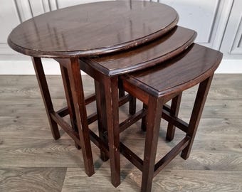 May include: Set of three nesting tables in varying sizes. The tables have a dark brown finish and a classic design. The largest table has an oval top, while the other two have curved edges. The tables are made of wood and have a sturdy, traditional look.
