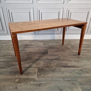 May include: A rectangular wooden table with a smooth, light brown grain finish. The table features a flat top surface and four straight, slightly tapered legs that extend outwards from the corners, providing a stable and balanced structure.