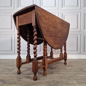 May include: A vintage wooden drop-leaf table with a warm brown finish. The table features a rectangular top with rounded edges and turned legs with a spiral design. The table is approximately 76 cm long when fully extended.
