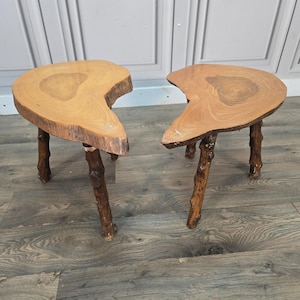 May include: Two side tables featuring natural live-edge wood slab tops with visible grain patterns and light brown tones. Each table is supported by three dark brown, textured branch-style legs that provide a sturdy base for the irregular wooden surfaces.