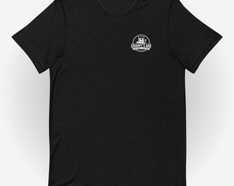 Puede incluir: Camiseta negra con un logotipo circular blanco que dice "Grumpy's Bar" encima de las palabras "The Drinks & The Food". El logotipo presenta una imagen estilizada de un edificio. La camiseta está hecha de un material suave.