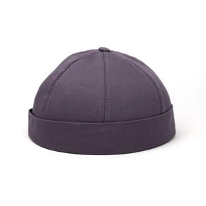 Puede incluir: Un gorro docker gris oscuro con una visera corta. El gorro tiene una corona redondeada con costuras verticales. Este gorro informal está hecho de una tela resistente y es adecuado para el uso diario. Un accesorio versátil.