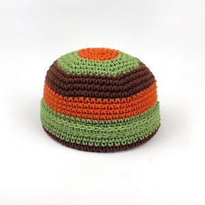 May include: A crocheted beanie hat with a striped pattern in shades of green, brown, and orange. The hat has a rounded crown and a folded brim. The colour scheme is earthy and vibrant, suitable for casual wear.