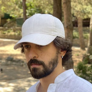 Op de afbeelding: Een lichtbeige baseballpet met een gebogen klep. De pet is gemaakt van een textuurstof en heeft een klassiek zes-panelen ontwerp. De pet heeft een neutrale kleur en is geschikt voor diverse outfits.