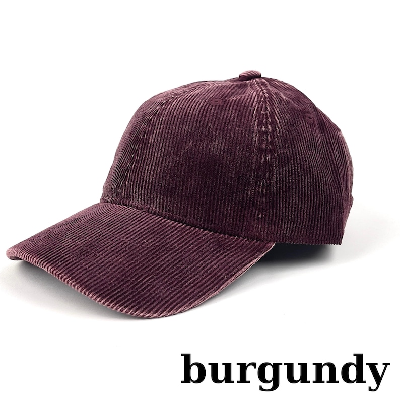 May include: Burgundy corduroy baseball cap with a curved brim. The cap is made of a ribbed fabric and has a rounded crown. The word "burgundy" is printed in a bold, sans-serif font at the bottom of the image.