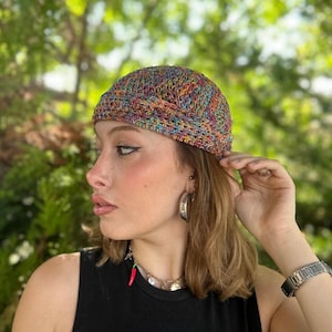 May include: A colorful, hand-crocheted beanie hat. The hat features a mix of rainbow colors, including red, yellow, blue, and green. The hat is worn by a person. The hat is a stylish accessory for any season.