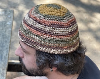 Puede incluir: Un gorro tejido a ganchillo hecho a mano. El gorro presenta un patrón circular en tonos tierra, incluyendo verde oliva, marrón y beige. El gorro tiene un borde acanalado y una corona redondeada. Adecuado para todos los géneros.