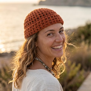 Puede incluir: Un gorro de ganchillo color óxido con un distintivo patrón de rejilla de tejido abierto y un borde grueso de punto sólido. El gorro presenta una corona redondeada y una construcción texturizada a base de hilo que se ajusta a la cabeza.