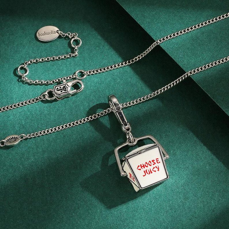 May include: Silver necklace with a chain and a pendant shaped like a Chinese takeout box. The box is white with red text that reads "CHOOSE JUICY". The necklace has a lobster clasp and a small tag that reads "boshuelin".