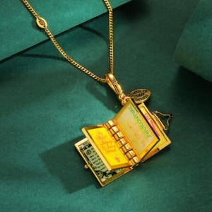 May include: Gold-toned necklace with a pendant shaped like an open book. The book pendant has detailed pages and the text "My Saltyness is Juicy Couture". The necklace has a delicate chain and a small charm that says "LIMITED 2009 EDITION".
