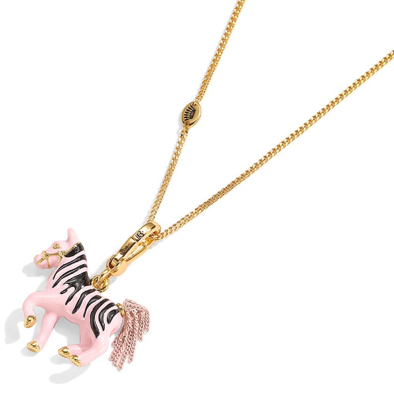 Puede incluir: Collar dorado con un colgante de cebra rosa y negro. El dije de cebra tiene un cuerpo rosa con rayas negras y una cola de borla rosa. El collar tiene una cadena delicada y un cierre de mosquet&oacute;n.