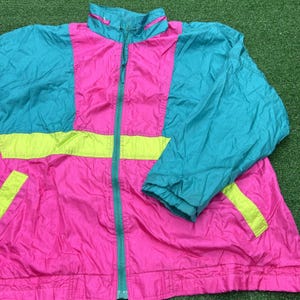 May include: A vintage, color-blocked jacket in a vibrant palette. The jacket features a bright pink base with teal blue and neon yellow accents. It has a full zipper, a stand-up collar, and long sleeves. The jacket is likely made of a lightweight, possibly nylon, material.