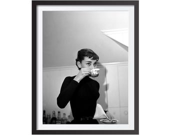 Op de afbeelding: Zwart-wit ingelijste print met een vrouw die uit een theekopje drinkt. De vrouw draagt een zwarte top. De theekop heeft een decoratief patroon. De afbeelding is een portret.