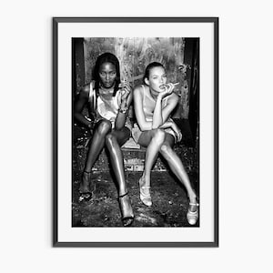 May include: Black and white framed print featuring two women seated, each holding a cigarette. They are wearing short dresses and heels. The image has a vintage, high-fashion aesthetic.
