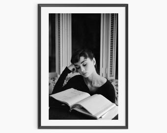 Op de afbeelding: Zwart-wit ingelijste print met een persoon die een boek leest. De persoon rust met het hoofd op de arm en kijkt naar het open boek. De achtergrond toont een raam.