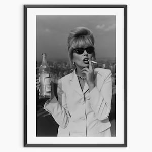 以下が含まれることがあります： サングラス、白いブレザー、シルバーのネックレスを身につけ、ボトルを持ちタバコを吸う女性の白黒フレームプリント。背景には都市景観が見えます。女性はブロンドの髪と赤い口紅をしています。