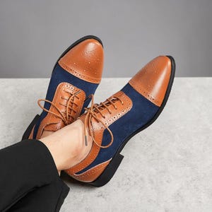 May include: Brown and navy blue leather dress shoes with a classic Oxford design. The shoes feature a perforated toe cap and side panels, with brown laces and a black sole. The shoes are a stylish choice for formal occasions.