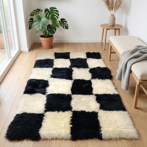 May include: A rectangular, checkered rug with alternating black and cream-colored squares. The rug has a shaggy texture and is placed on a light-colored wooden floor. The rug is a home decor item.
