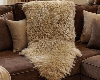 Könnte beinhalten: Eine beige Kunstfell-Wurfdecke liegt auf einem braunen Sofa. Die Decke hat eine zottelige Textur und ist von braunen und beigen Wurfkissen umgeben. Das Sofa hat eine dunkelbraune Farbe und schafft eine gemütliche und einladende Atmosphäre.