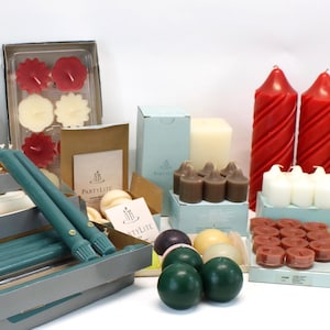 May include: A collection of candles in various shapes, sizes, and colors. Includes tall red spiral candles, teal taper candles, and small votive candles in boxes. There are also tealight candles and round green candles.