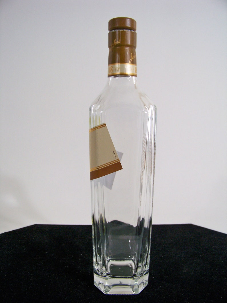 May include: A clear glass bottle with a brown cap and a gold label. The bottle is empty and has a rectangular shape.