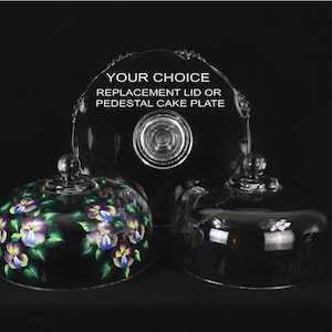 May include: Three glass cake domes and a pedestal cake plate are displayed against a black background. One dome is decorated with purple, yellow, and blue floral designs. The text "YOUR CHOICE REPLACEMENT LID OR PEDESTAL CAKE PLATE" is visible.
