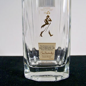 May include: A clear glass bottle with a label that reads "The Pursuit of the Ultimate 18 Year Old Blend" and "Jim Beveridge Master Blender Johnnie Walker".