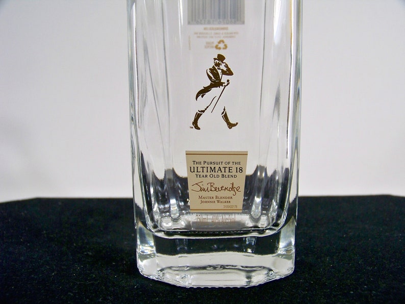 May include: A clear glass bottle with a label that reads "The Pursuit of the Ultimate 18 Year Old Blend" and "Jim Beveridge Master Blender Johnnie Walker".