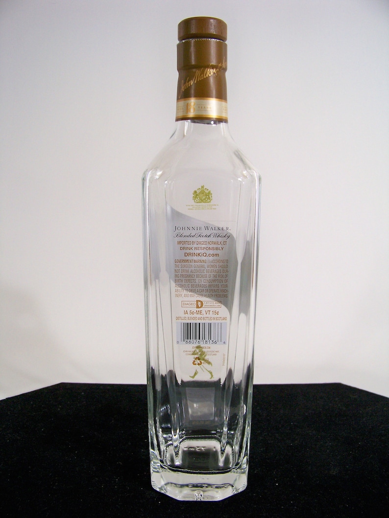 May include: A clear glass bottle of Johnnie Walker Blended Scotch Whisky. The bottle has a gold label with the Johnnie Walker logo and text. The label also includes the government warning about alcohol consumption during pregnancy. The bottle is sitting on a white surface.