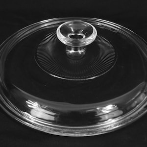 May include: A clear glass lid with a knob on top. The lid has a raised, textured rim.