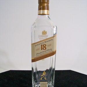 May include: A clear glass bottle of Johnnie Walker 18 year old blended Scotch whisky. The bottle has a gold label with the Johnnie Walker logo and the words "Aged 18 Years".
