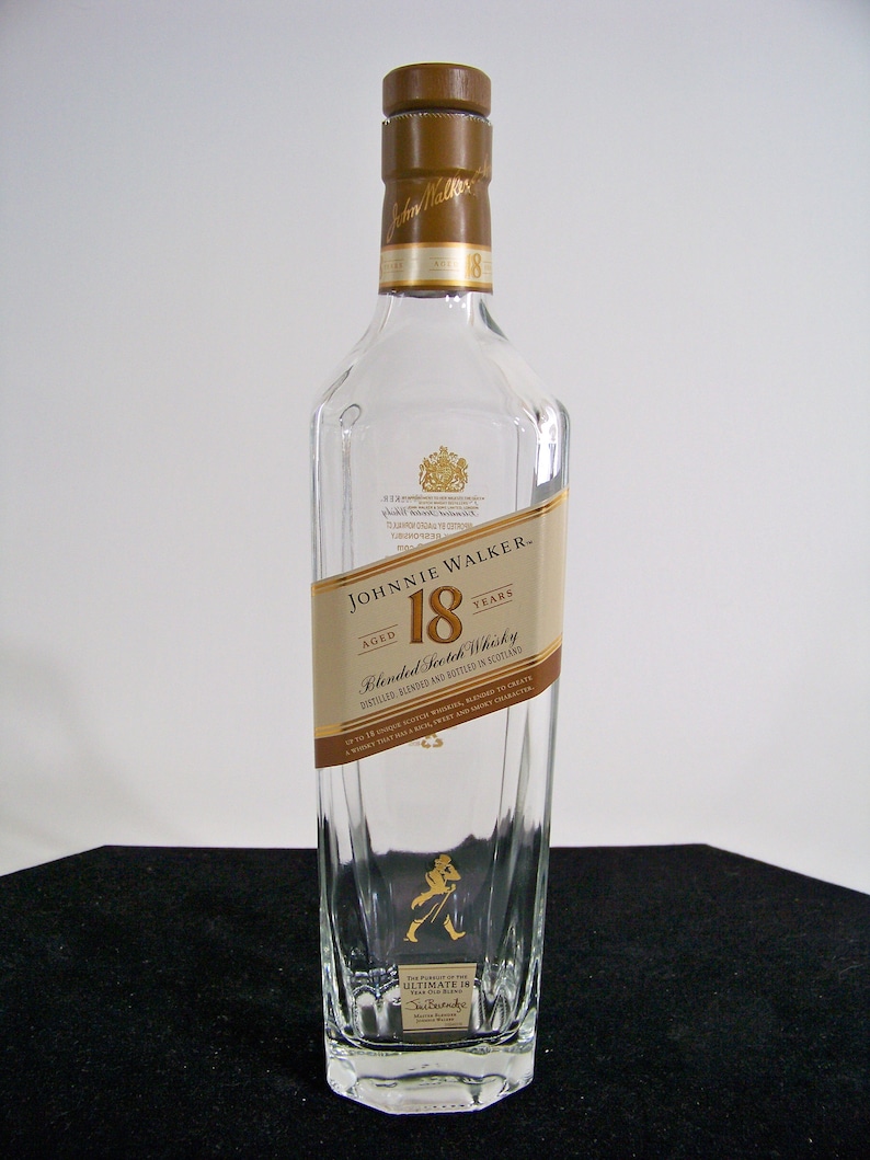 May include: A clear glass bottle of Johnnie Walker 18 year old blended Scotch whisky. The bottle has a gold label with the Johnnie Walker logo and the words "Aged 18 Years".