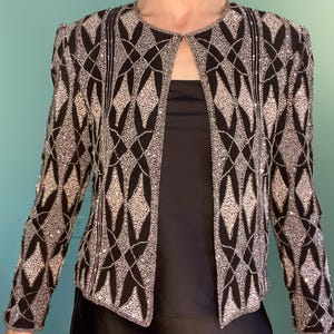 May include: Black jacket with a geometric pattern of silver beads and sequins. The open-front jacket has long sleeves and a round neckline. The jacket is embellished with a diamond pattern.