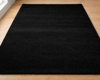 May include: A rectangular area rug featuring a solid black color and a dense, plush pile texture. The rug is positioned flat, showcasing a uniform surface appearance with consistent dark tones throughout the entire rectangular textile piece.