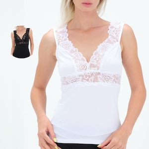 Könnte beinhalten: Weißes Tanktop mit V-Ausschnitt und zarter weißer Spitzenborte am Ausschnitt und an der Brust. Ein kleineres Bild eines schwarzen Tanktops mit Spitzenbesatz befindet sich in der oberen linken Ecke. Das Tanktop ist ärmellos.