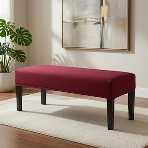 May include: A rectangular bench featuring a deep red, textured fabric cover with a subtle diamond-shaped pattern. The bench is supported by four straight, dark brown wooden legs, providing a stable base for this piece of furniture.