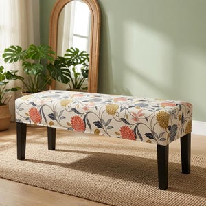 May include: A rectangular bench featuring a cream-colored fabric cover with a floral pattern in shades of orange, yellow, blue, and grey. The bench is supported by four straight, dark brown wooden legs, providing a stable base for the seat.