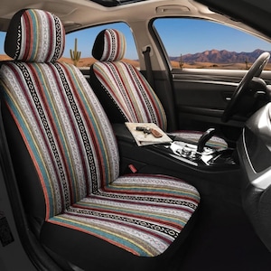 May include: Car seat covers featuring a vibrant striped design in shades of red, blue, yellow, and white. The covers are fitted in a car, with a desert scene visible through the windows. The headrests and seat cushions are covered.