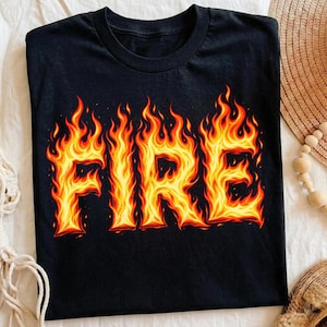 Op de afbeelding: Een zwart t-shirt met korte mouwen waarop het woord FIRE is gedrukt in een levendige, gestileerde vlammenafbeelding. De letters bestaan uit felgele, oranje en rode vlammen die contrasteren met de donkere stof van het kledingstuk met ronde hals.