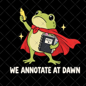 May include: A green frog wearing a red cape, holding a yellow highlighter and a black spiral-bound notebook labeled NOTES with a heart icon. The text WE ANNOTATE AT DAWN is printed below the frog against a black background with small yellow stars.