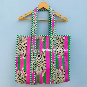 May include: A colourful tote bag with a tiger print. The bag has pink and green vertical stripes, with tiger illustrations. The handles and edges are trimmed with a white and green striped pattern. The text "Heritage Weaves Co." is visible on the bag.