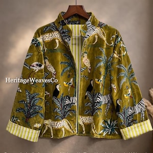 Pode incluir: Casaco de veludo verde-oliva com estampa de tema de selva com leopardos, zebras, pássaros e palmeiras. O casaco tem fecho de correr frontal e punhos listrados. O nome da marca "Heritage WeavesCo" é visível.