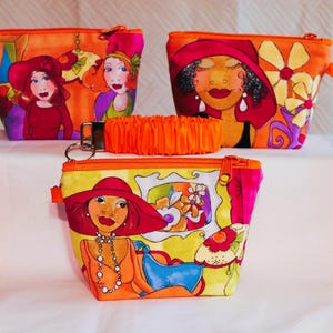 May include: Three fabric pouches with zipper closures and matching orange ruffled wrist straps. Each pouch features a colorful graphic print of stylized figures wearing hats, accented with floral patterns in shades of orange, yellow, and pink.